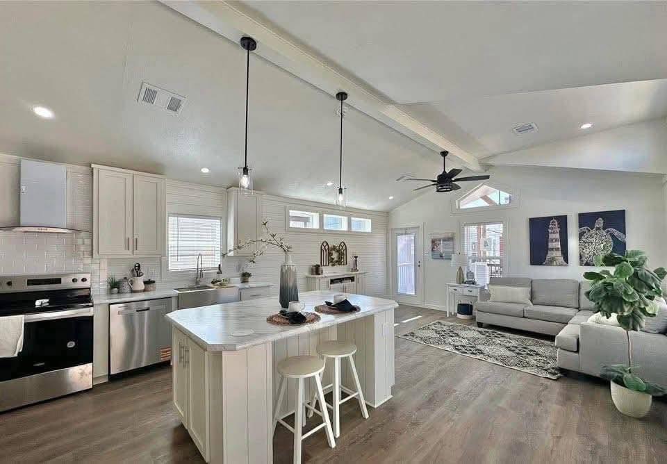 Modern, airy kitchen and living room with high ceilings and wooden floors. A marble island with stools, sleek appliances, a beige sofa, and stylish decor create a warm, inviting space.