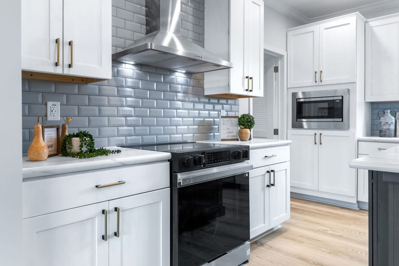 Sleek kitchen with white cabinets, stainless steel appliances, and a glossy gray subway tile backsplash. Wooden accents add warmth and modernity.