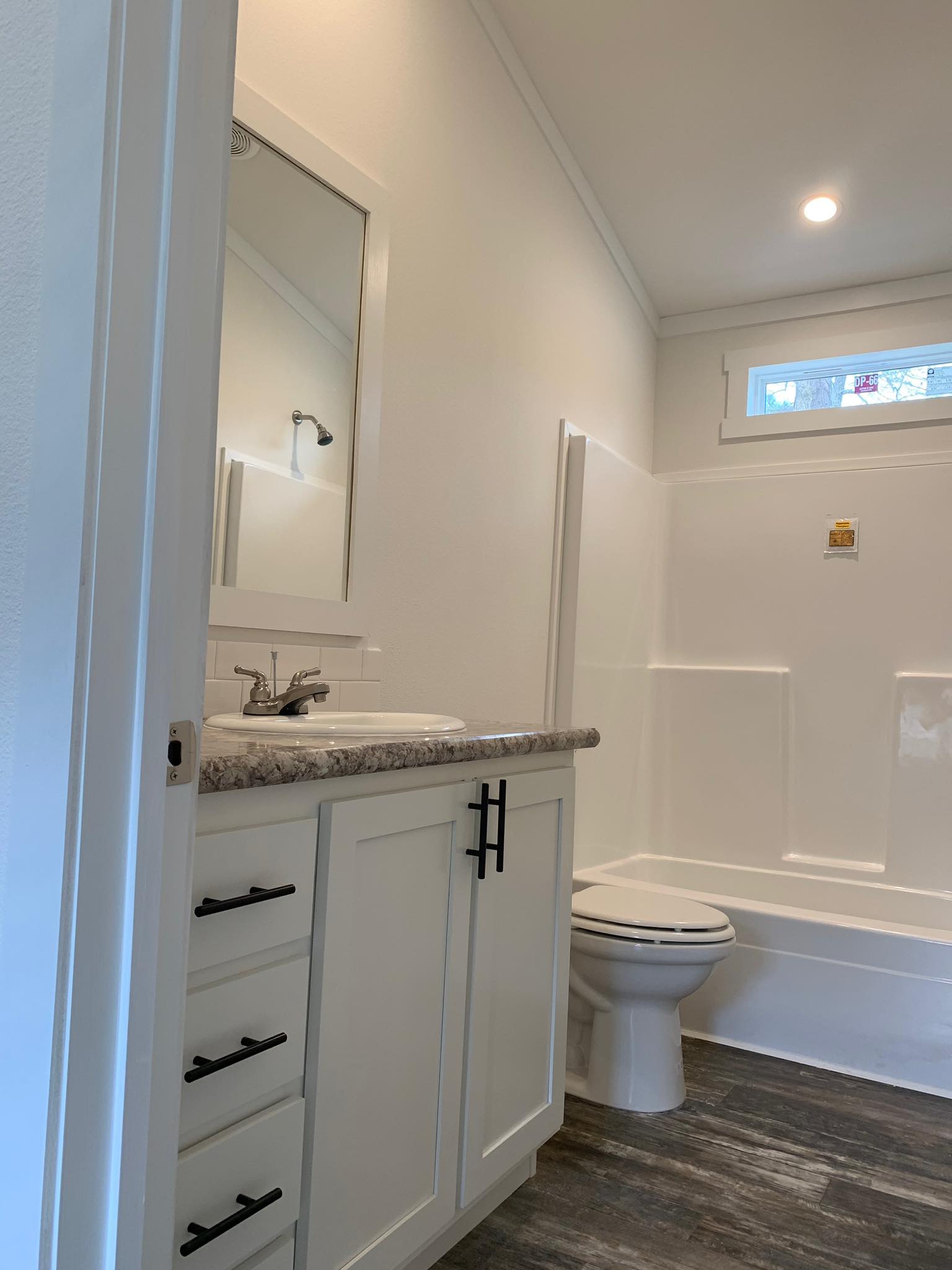 Compact bathroom with white walls, a granite countertop, and black-handled cabinets. Includes a mirror, sink, toilet, and a shower-tub combo.