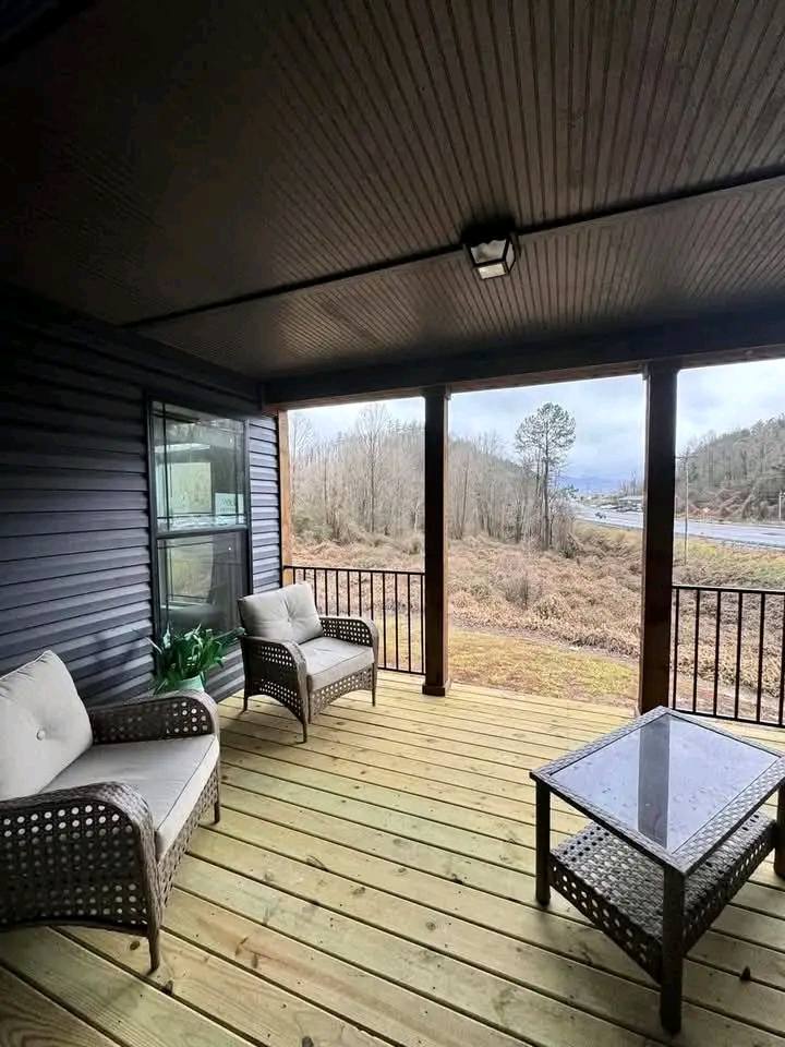 A cozy covered porch with rattan chairs and cushions, a glass-topped table, and a potted plant. It overlooks a serene, bare winter landscape.