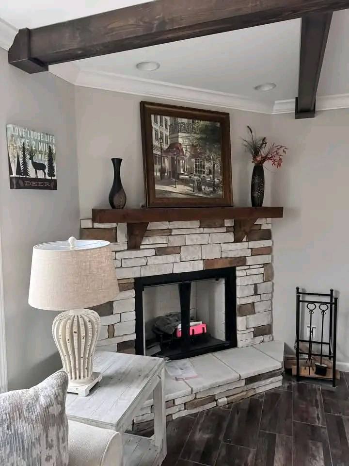 Cozy living room with a stone fireplace, wooden mantel, and framed art above. A table lamp sits on a side table, creating a warm, inviting atmosphere.