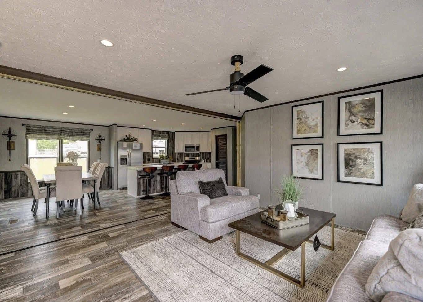 Spacious open-plan living area with gray couches, a modern coffee table, and textured rugs. Dining area and kitchen bar with stools in the background. Neutral tones and artwork create a cozy, contemporary vibe.