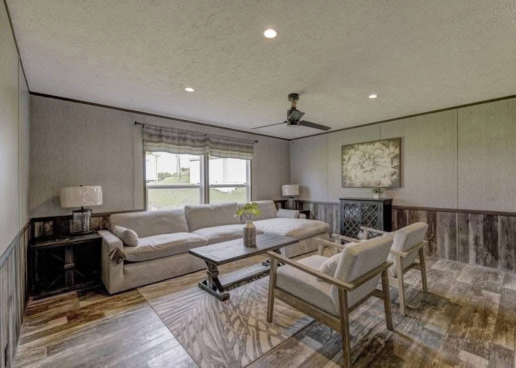 Cozy living room featuring gray walls, a large beige sectional sofa, a wooden coffee table, and two armchairs. A floral painting and soft lamps add warmth.
