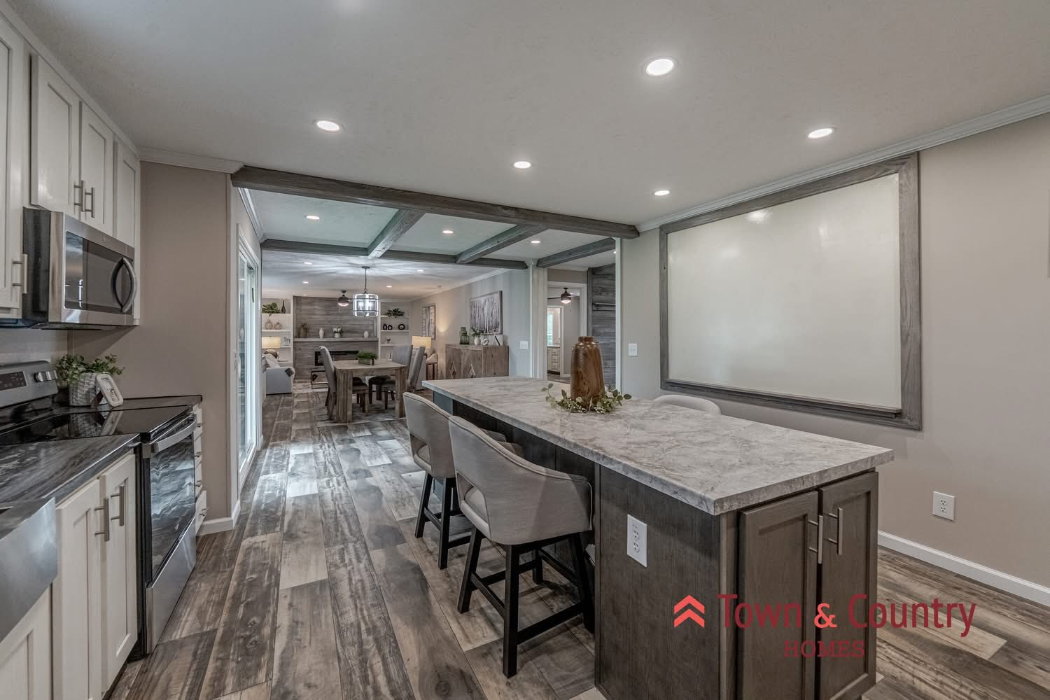 Modern kitchen with a long island, marble countertop, and cushioned bar stools. Open layout leads to a dining area. Neutral tones, cozy ambiance.