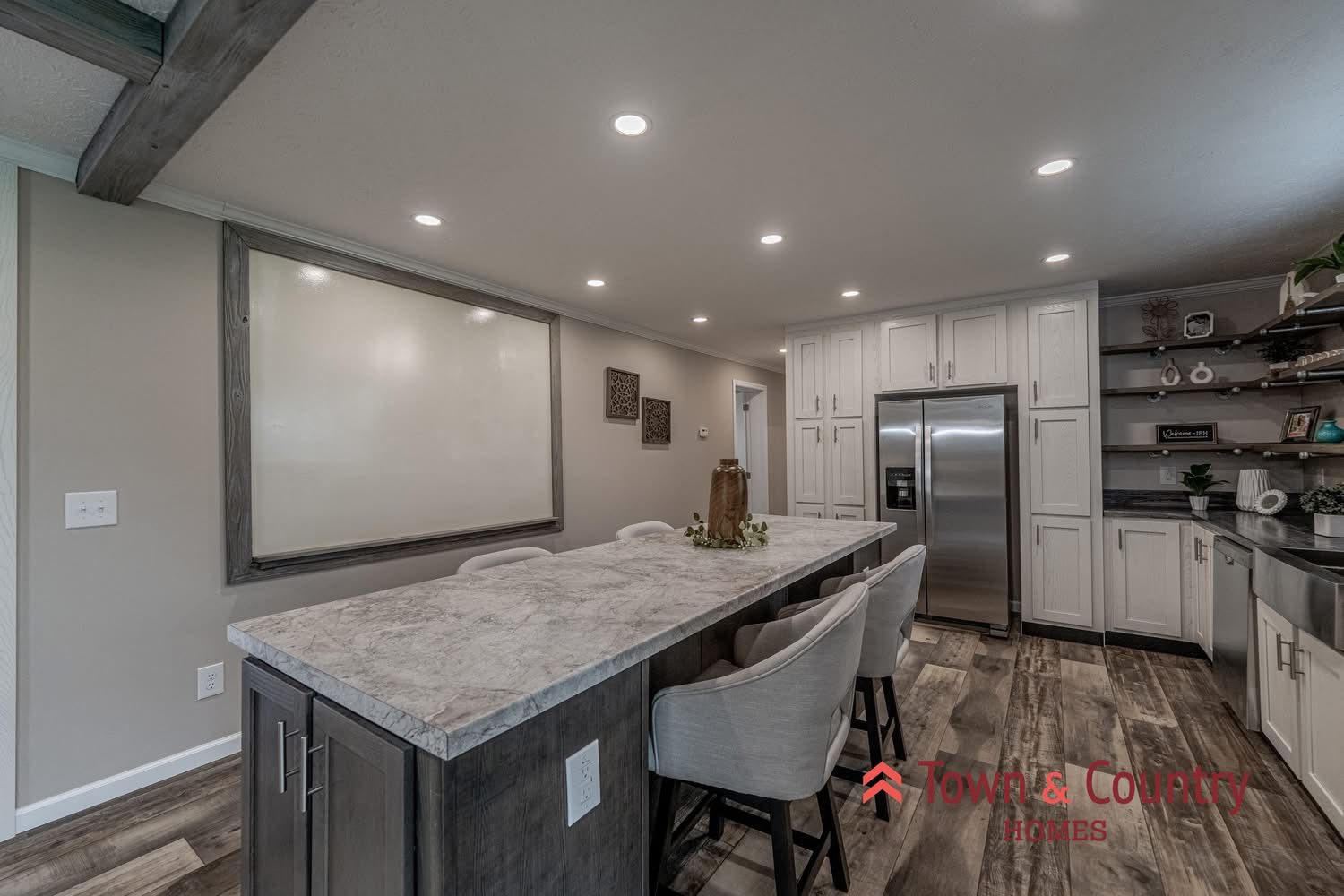 Modern kitchen with sleek white cabinets, marble countertops, and stainless steel appliances. Features a large central island with gray chairs and warm lighting.