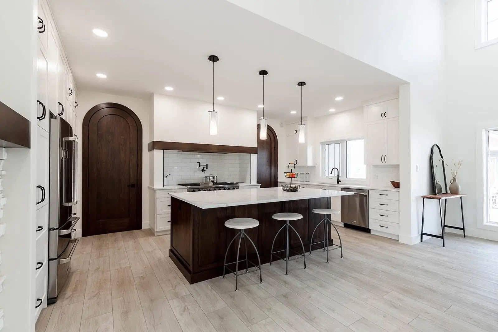 Stylish kitchen with a central island featuring three stools and pendant lights. White cabinets, stainless steel appliances, and wooden accents create a modern, inviting atmosphere.