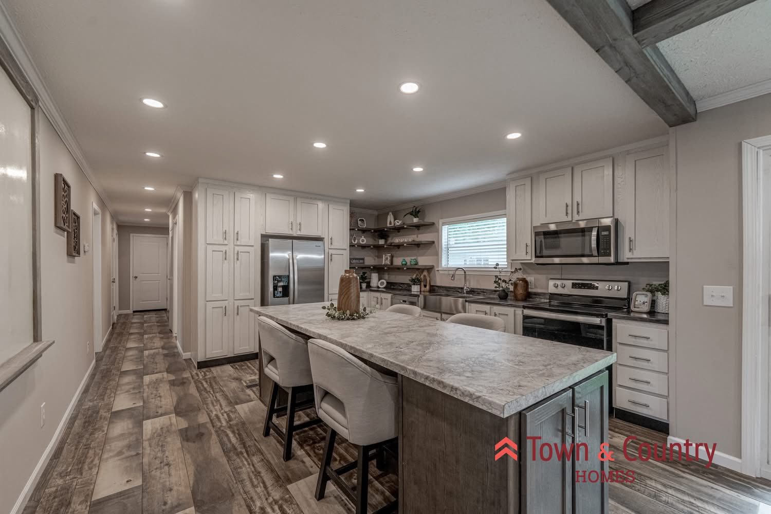 Spacious kitchen with rustic wood floors, a large island, modern appliances, and open shelving. Warm lighting creates a cozy, welcoming ambiance.