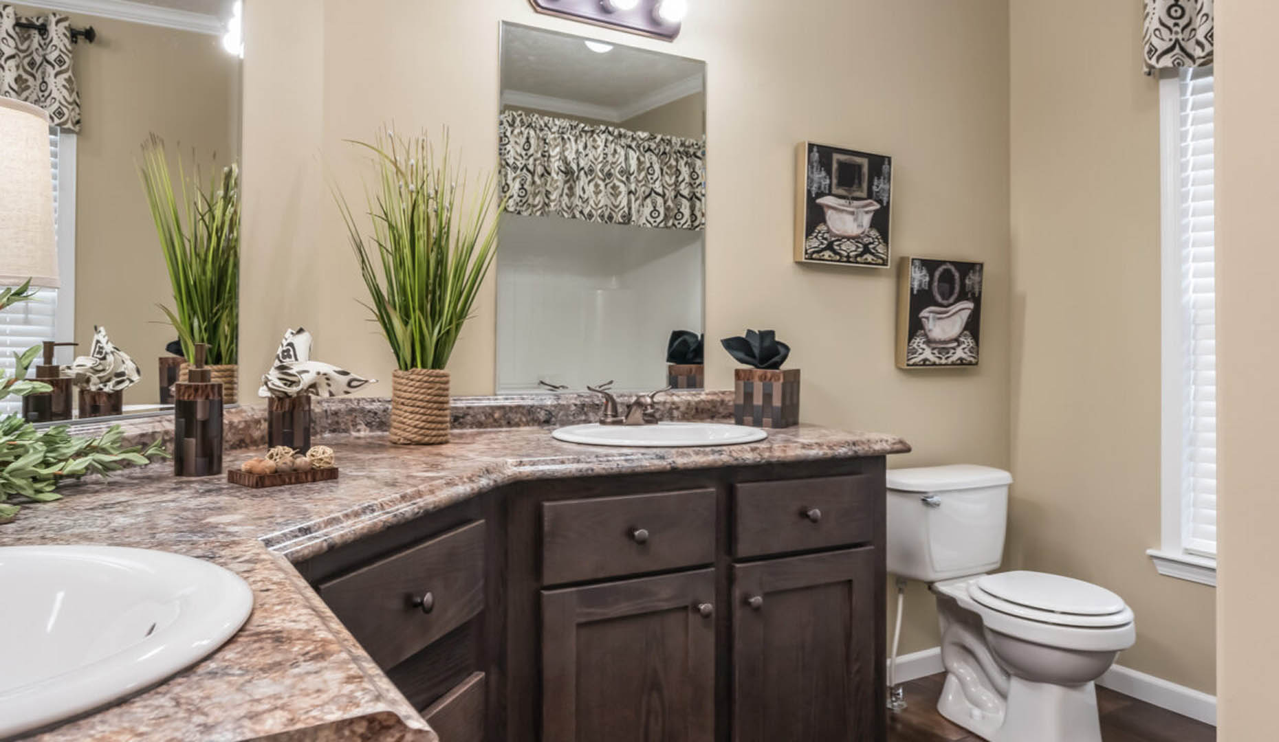 A modern bathroom with a beige color scheme, featuring a dual-sink vanity with a marble countertop, decorative plants, and a toilet. The atmosphere is clean and inviting.