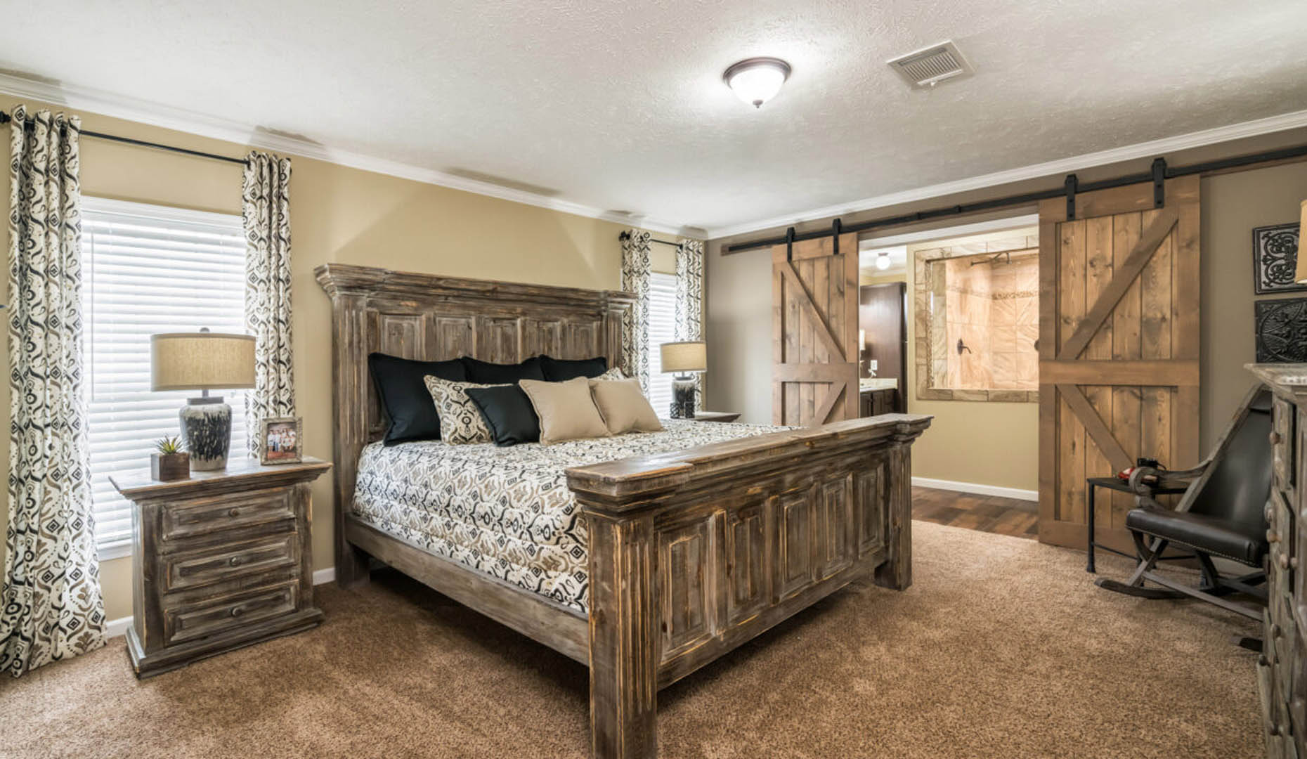 A cozy bedroom featuring a rustic wooden bed with patterned bedding, matching nightstands with lamps, barn-style sliding doors, and soft lighting.