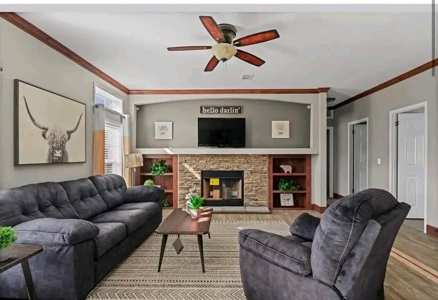 Cozy living room with grey sofas, a wooden coffee table, and plants. A fireplace with a "hello darlin'" sign and TV above, creating a welcoming vibe.