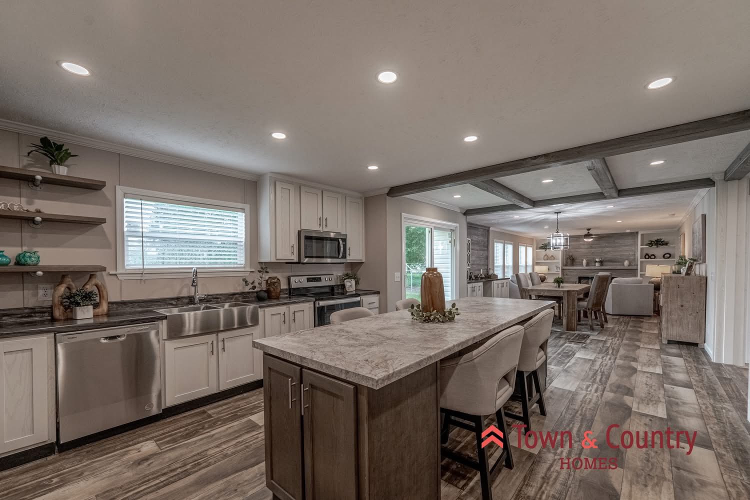 Stylish open kitchen with modern appliances, center island, and bar stools. Warm wooden tones and recessed lighting create an inviting atmosphere.
