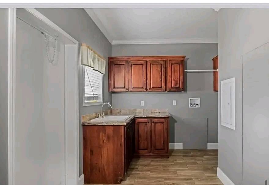 Laundry room with wooden cabinets, a marble countertop with sink, tile flooring, and gray walls. A small window lets in natural light.