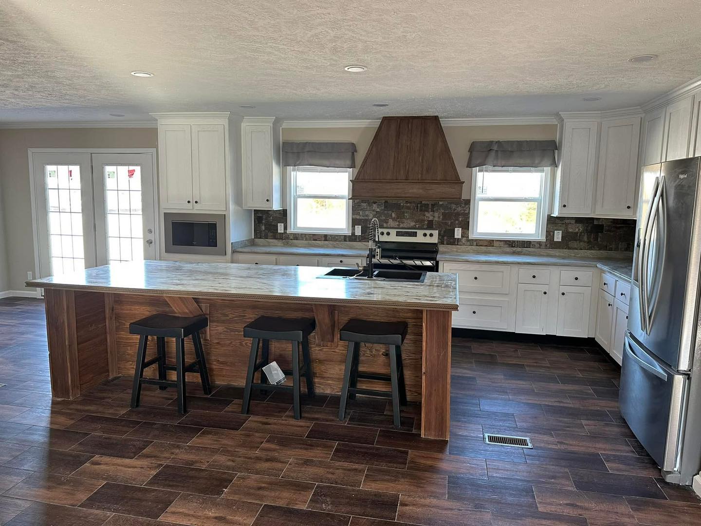 Modern kitchen with a large wooden island, marble countertop, and three stools. White cabinets and stainless steel appliances create a sleek, warm atmosphere.