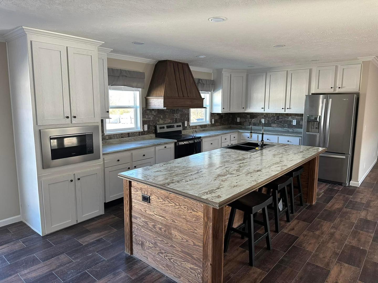 Modern kitchen with a large marble island, wooden cabinets, stainless steel appliances, and dark wood floors. Bright and spacious ambiance.