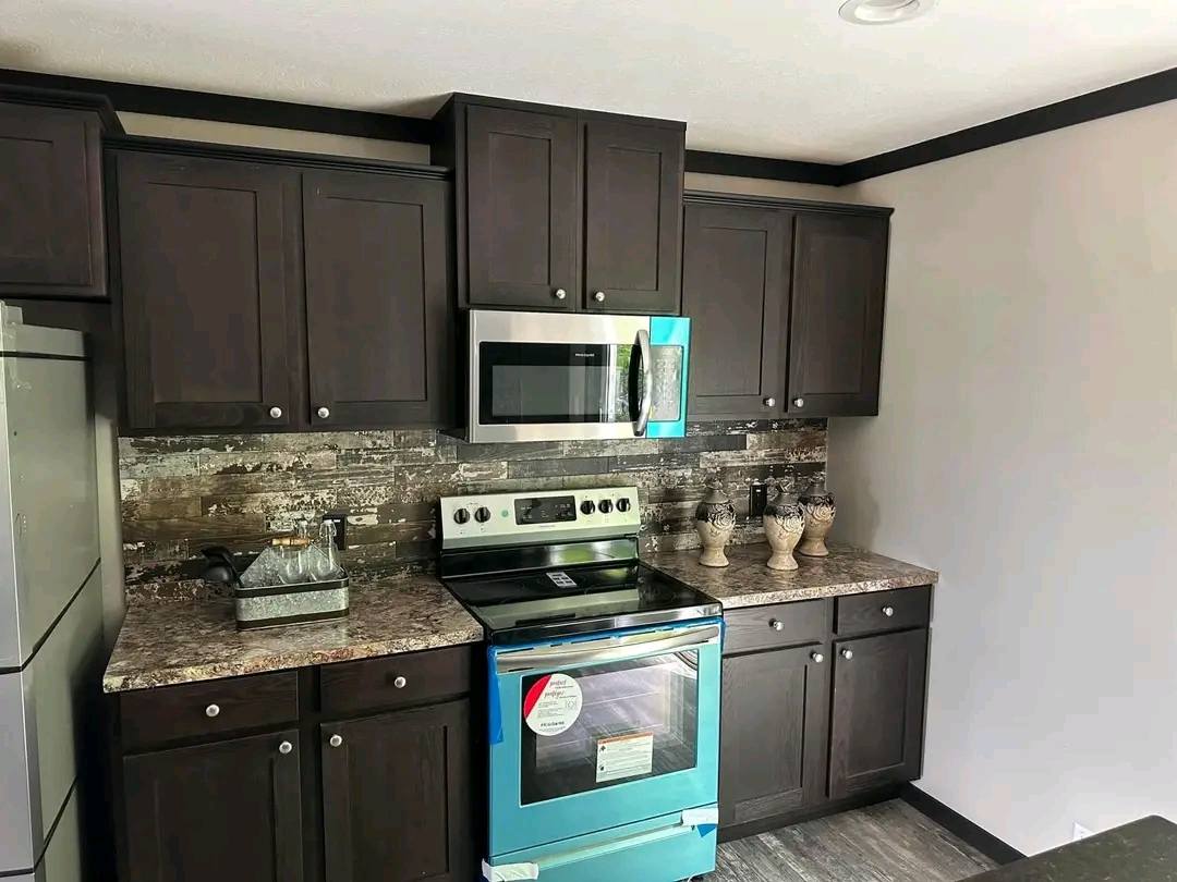 Modern kitchen with dark wood cabinets and a stainless steel stove and microwave. The backsplash has a rustic design, and the countertops are granite.