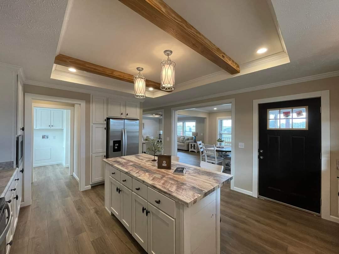 Stylish kitchen with a wood beam ceiling, large island with marble countertop, pendant lights, stainless steel appliances, and a warm, inviting open-plan layout.