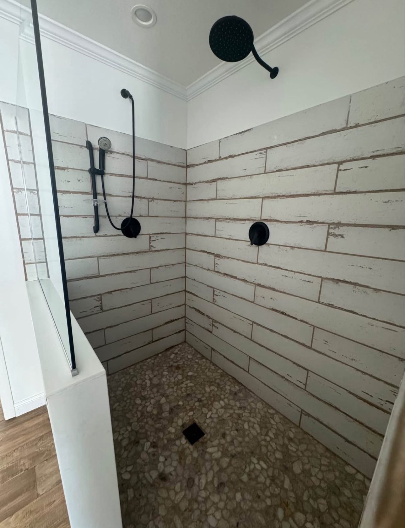 Spacious shower with textured stone tiles and black fixtures on one wall. Pebble stone flooring contrasts with white wall tiles, creating a modern feel.