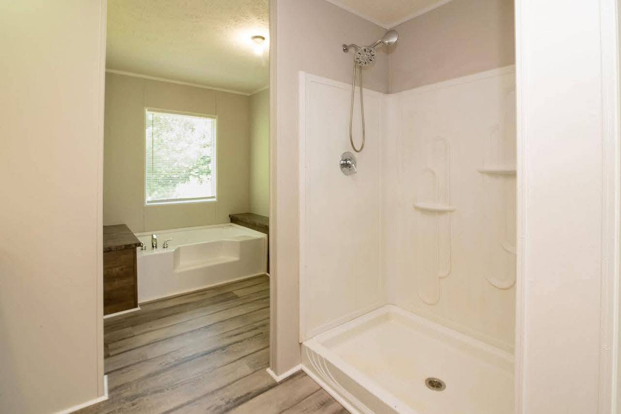 Modern bathroom with light wood floor, featuring a white shower stall, a large bathtub with wooden trim, and a window allowing natural light.