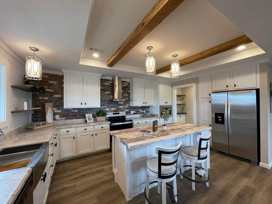Modern kitchen with white cabinets, stainless steel appliances, and a central island with two bar stools. Warm wood accents and pendant lights add coziness.