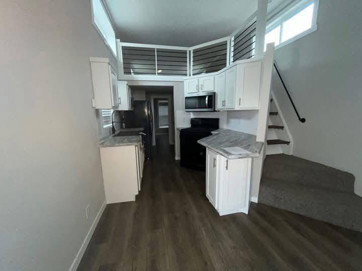Cozy kitchen with white cabinets, stainless steel appliances, and dark wood flooring. A small staircase leads to an upper loft with railing.
