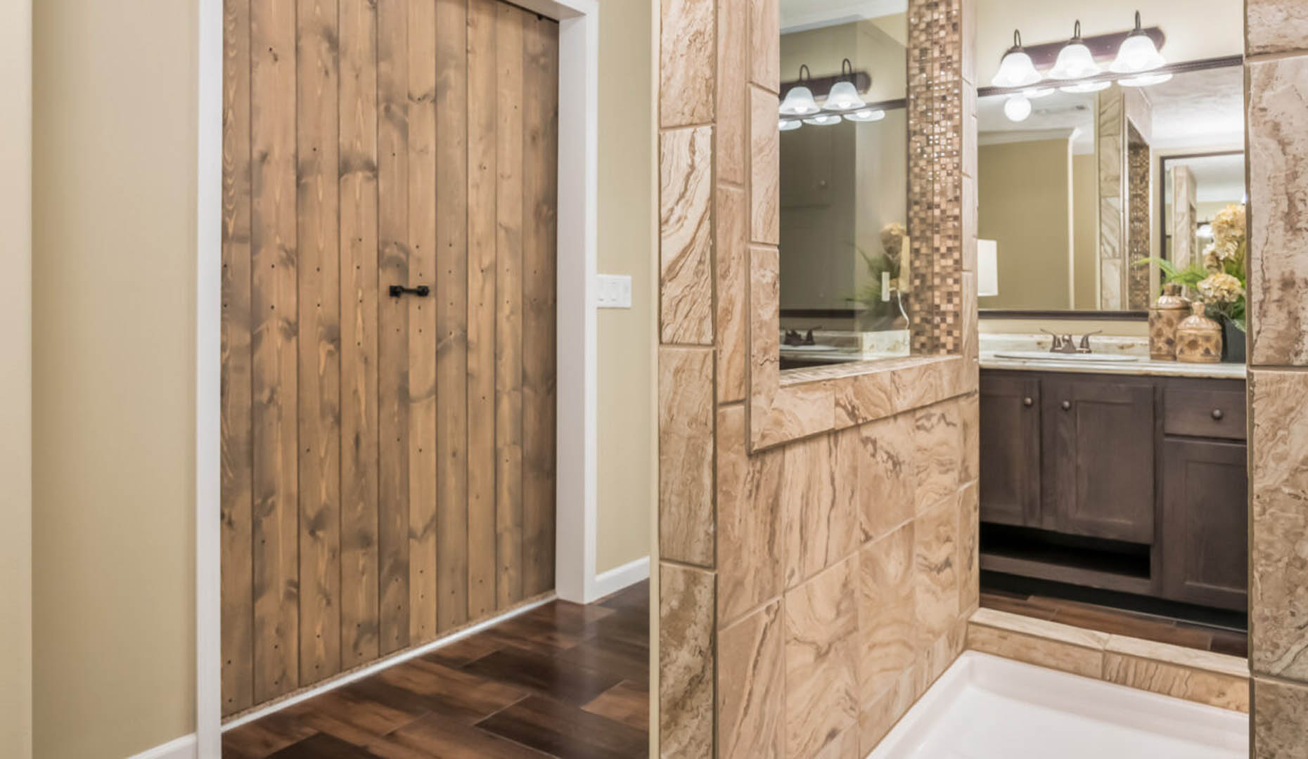 Modern bathroom with a natural wood sliding door and stone-tiled shower. Dark vanity with mirrors and soft lighting, creating a warm, inviting ambiance.