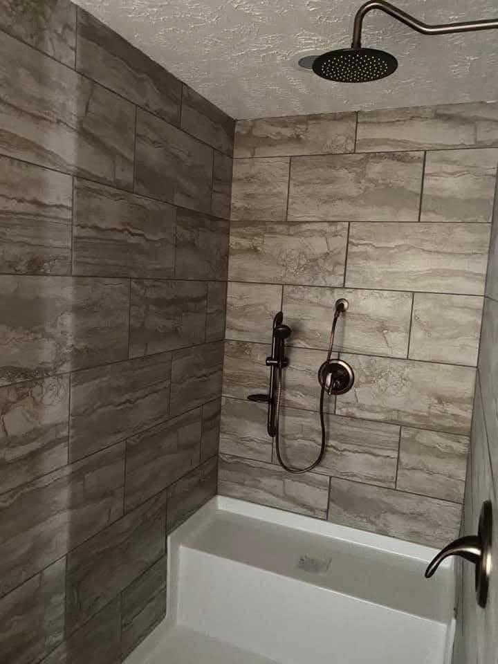 A modern shower with gray stone tiles and a ceiling-mounted rain showerhead. A handheld shower attachment is mounted on the wall, adding a sleek touch.