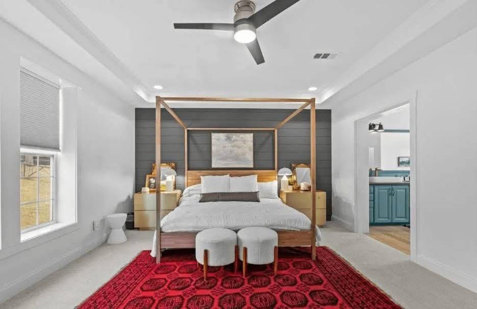 Spacious bedroom with a canopy bed, white and gray color scheme, bold red rug, and elegant bedside lamps, conveying a modern, tranquil vibe.