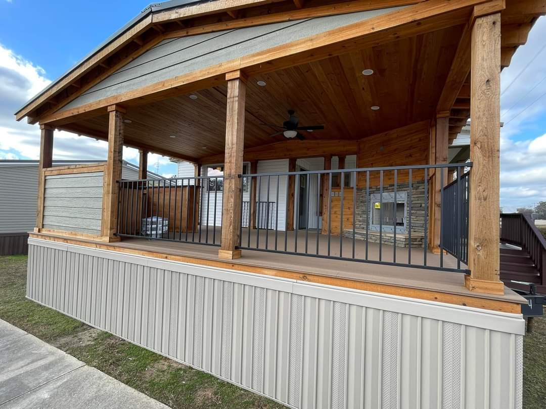 Spacious wooden porch with a sloped roof, featuring sturdy columns and black railings. A ceiling fan and stone fireplace add rustic charm.