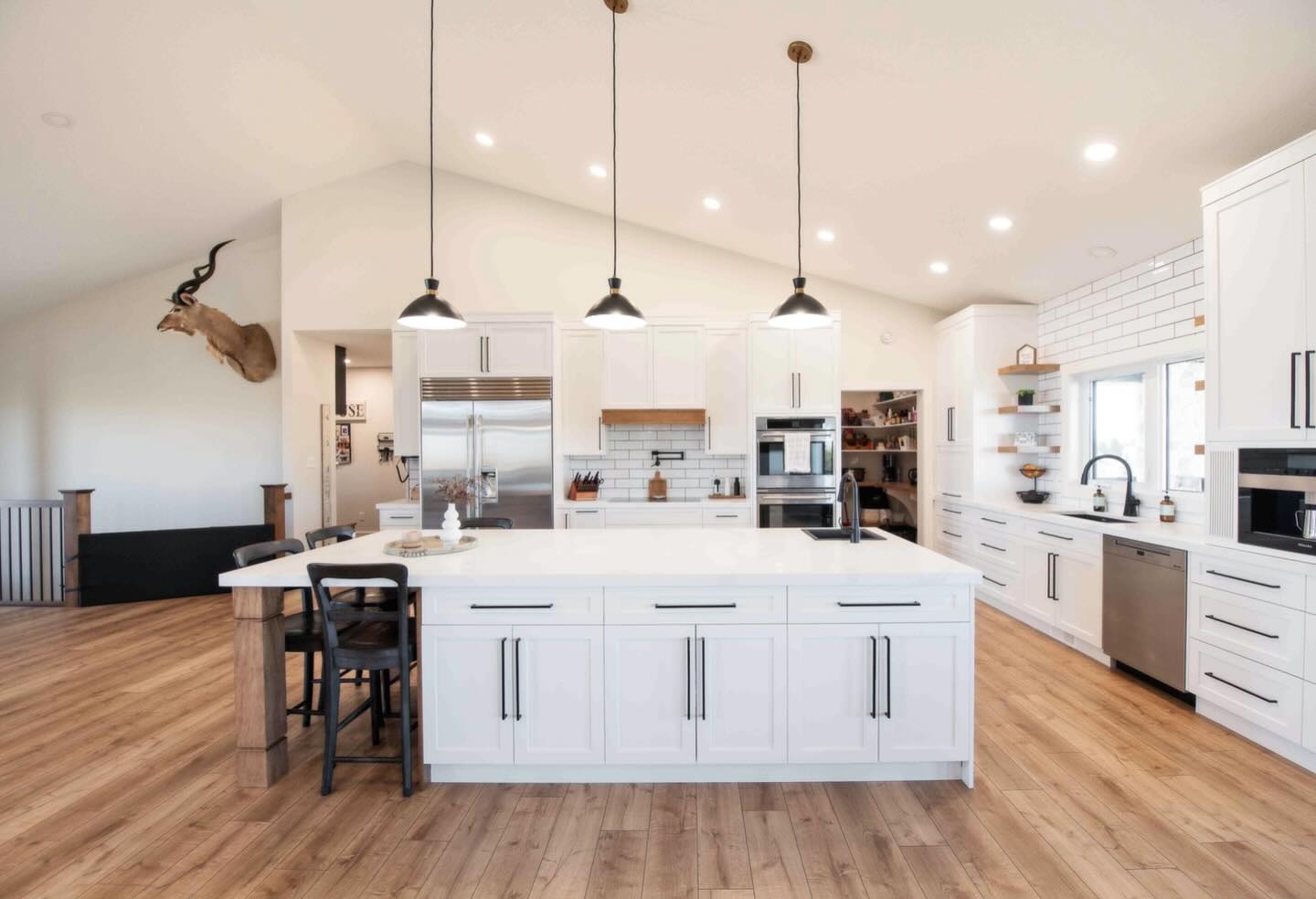 Spacious modern kitchen with white cabinets, large island, and pendant lights. Wood floors, stainless steel appliances, and a mounted antelope head create a stylish, inviting atmosphere.