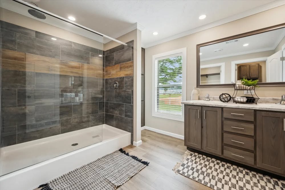 Modern bathroom featuring a glass-enclosed shower with dark tiles and wood accents, a large mirror above a wooden vanity, and natural light from a window.