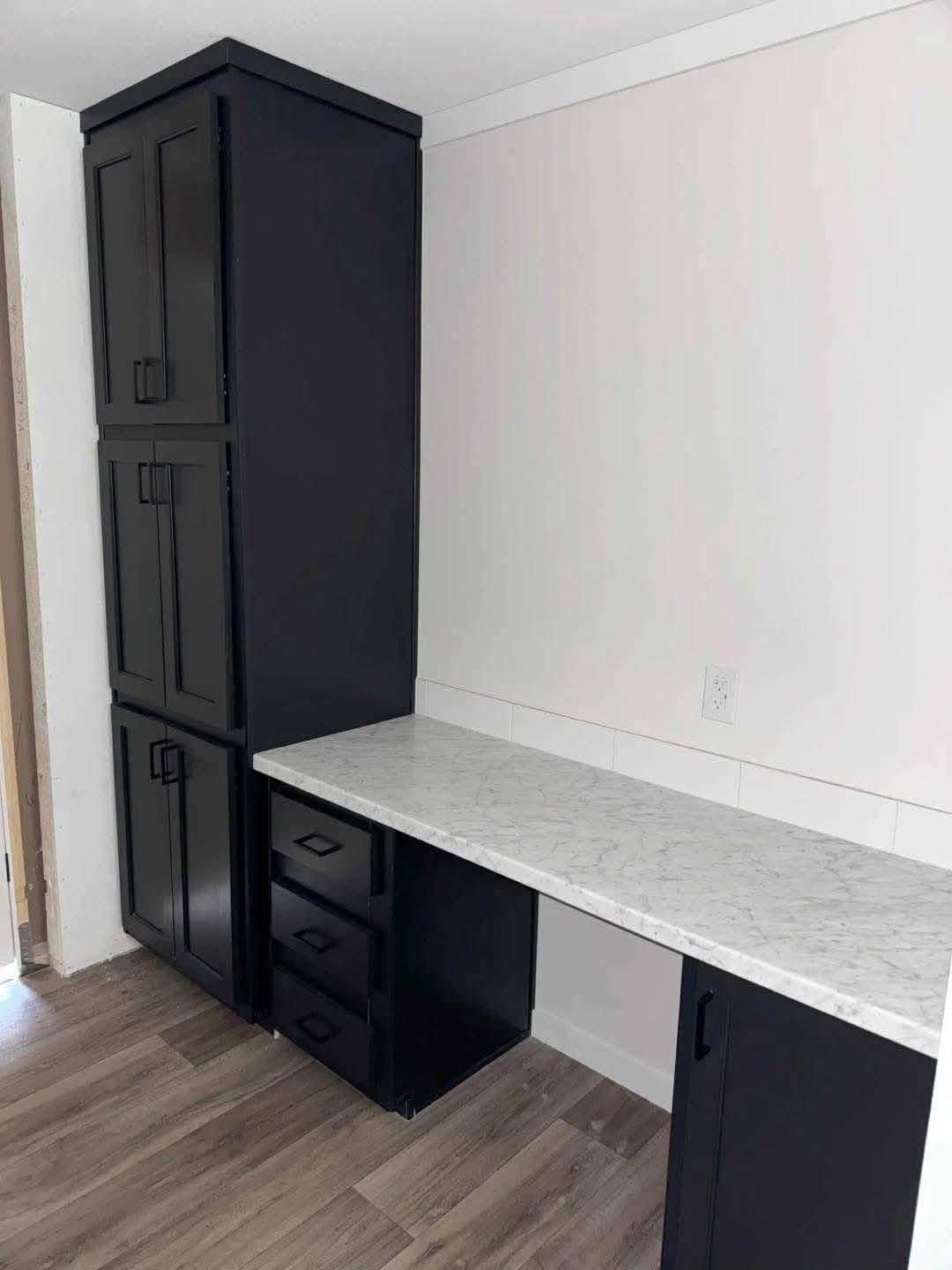 Modern office nook with black cabinets, white marble countertop, and wood flooring. Sleek, minimalist design creates a clean, organized workspace.