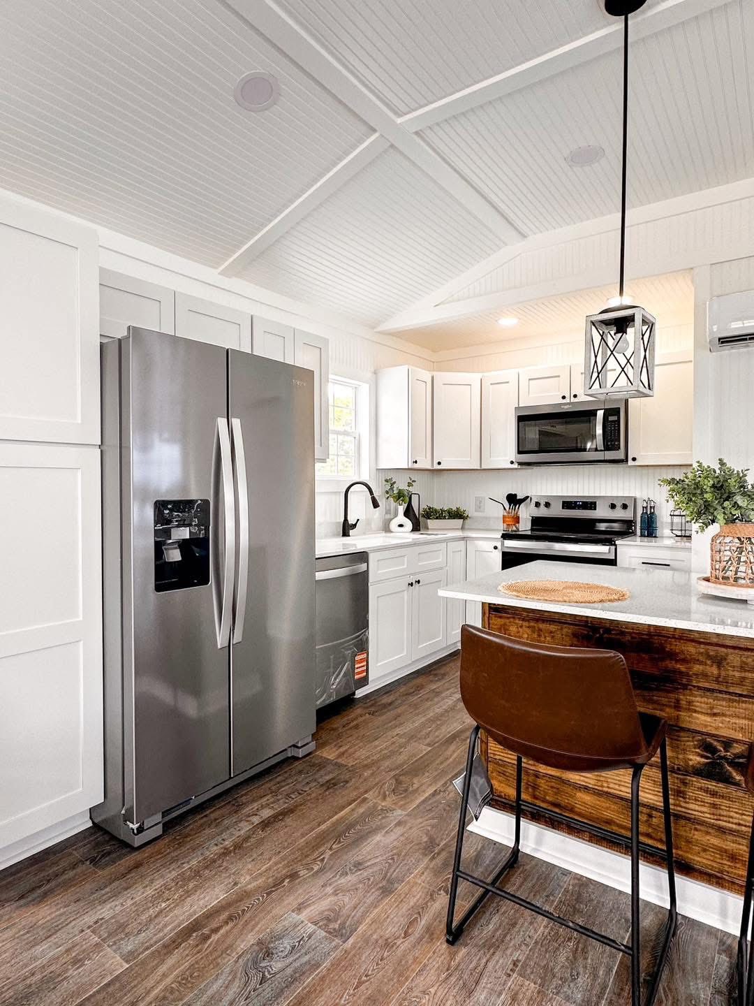 Bright kitchen with sleek stainless steel appliances, white cabinets, and wood accents. Large fridge, peaceful ambiance, modern pendant light.