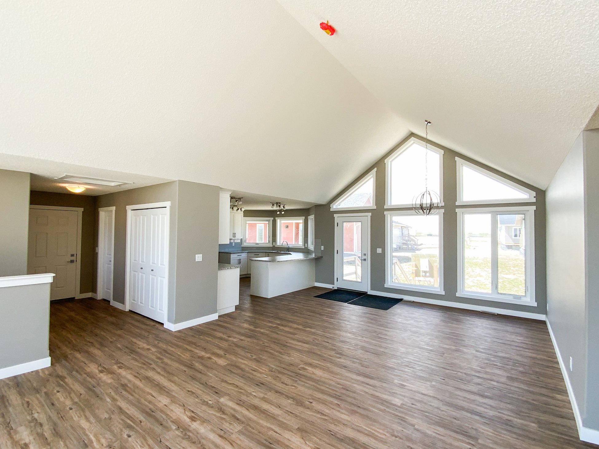 Spacious, modern living area with vaulted ceilings and large triangular windows. Light gray walls, wood floors, and a bright, airy atmosphere.