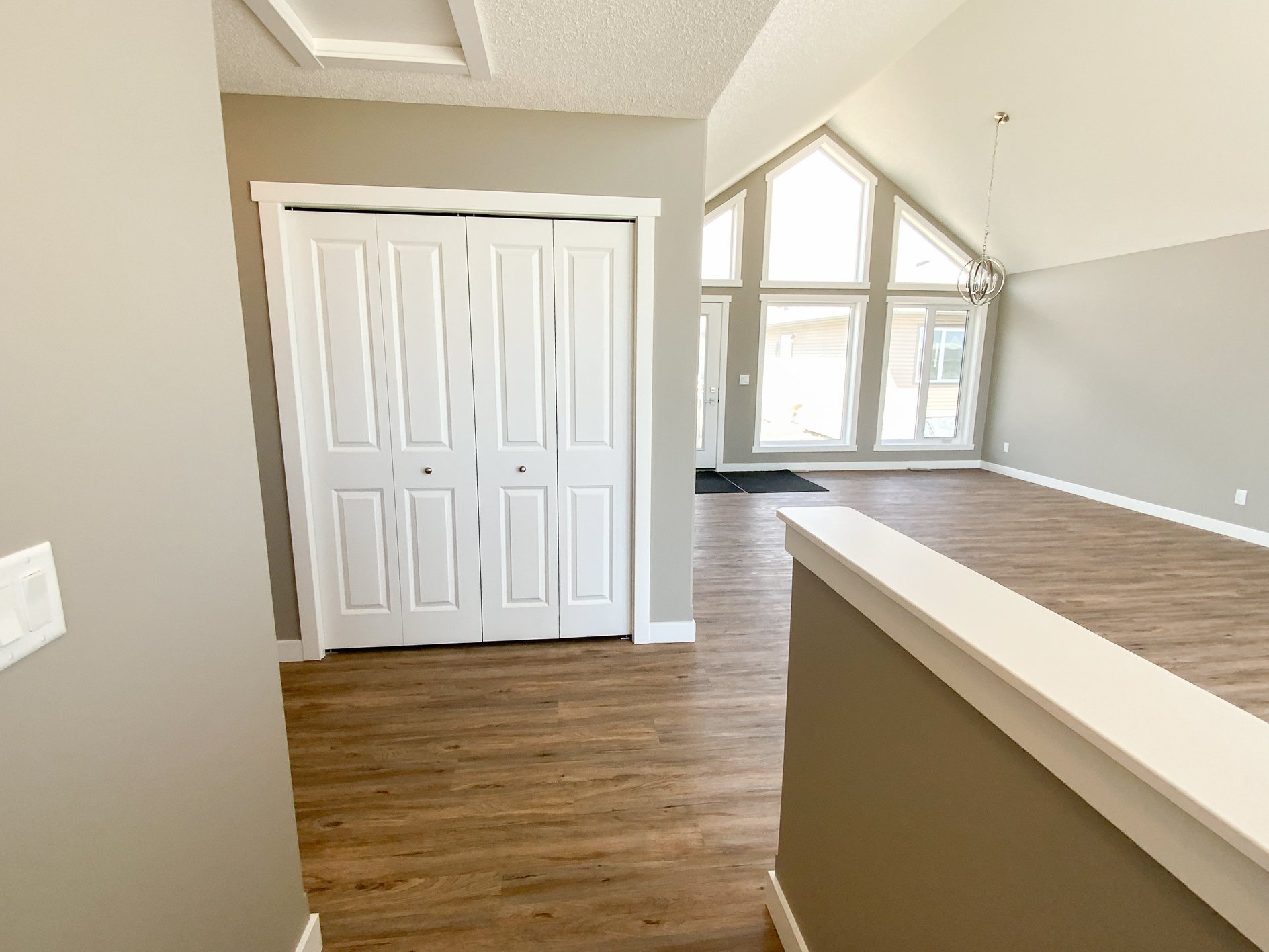 Spacious, modern room with vaulted ceiling, large triangular windows, wood flooring, and a white closet door, conveying an airy, minimalist vibe.
