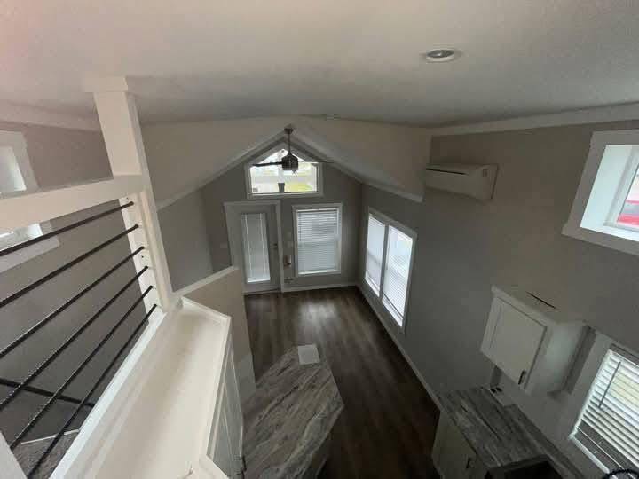 View of a small, modern living space from above with high ceilings, wood flooring, wide windows, a kitchen area, and glass doors leading outside.