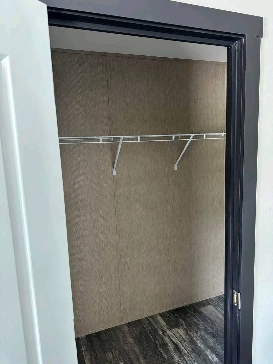 An empty walk-in closet with a gray door frame, beige walls, and a single white wire shelf. The floor is dark wood laminate, creating a clean, minimalist look.
