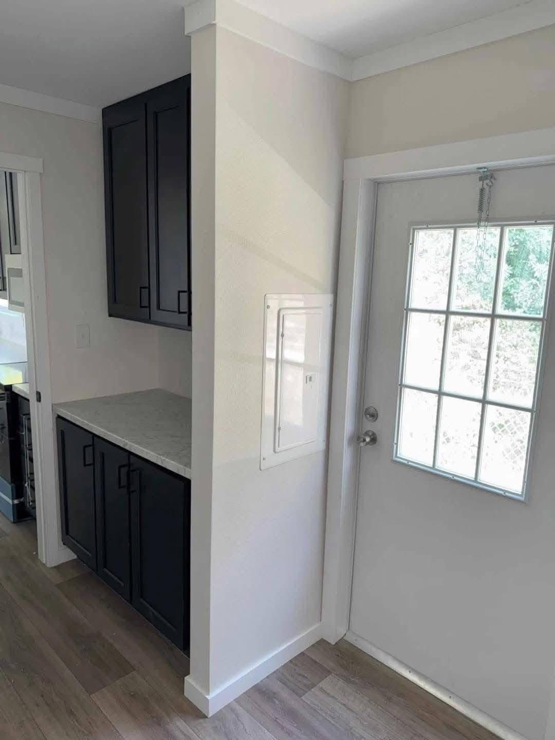 Small, bright kitchen nook with dark cabinets and a marble countertop next to a door with glass panels, creating a minimalist and cozy feel.