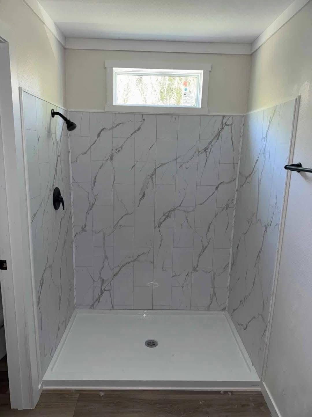Bathroom with a marble-tiled shower featuring a black showerhead and towel bar. A small window above lets in natural light, creating a calm ambiance.