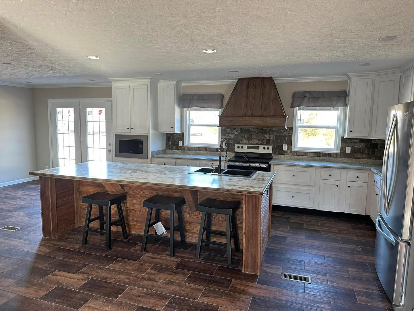 Spacious modern kitchen with a central island, marble countertop, and three black stools. White cabinets, stainless steel appliances, and natural light fill the room.