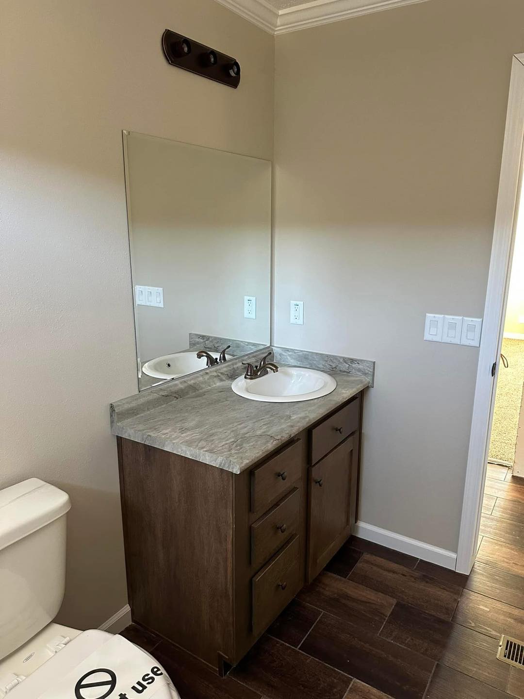 Compact bathroom with a wooden vanity cabinet and marble countertop. Single sink under a large mirror. Neutral tones, clean and minimalist design.