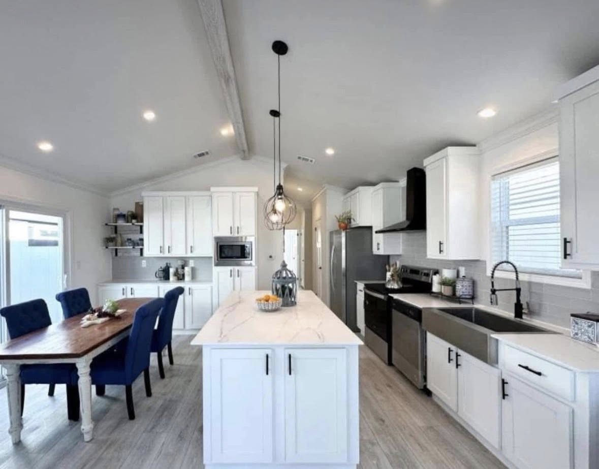 Modern kitchen with white cabinets, marble island, and stainless steel appliances. Blue chairs surround a wooden dining table, creating a cozy, inviting atmosphere.