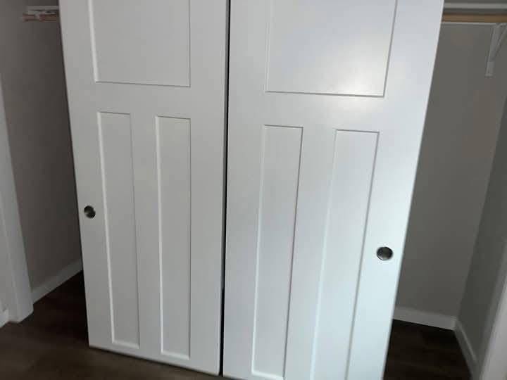 Closed white sliding closet doors with vertical panels, set against a neutral wall. The closet interior is partially visible, creating a tidy, serene ambiance.