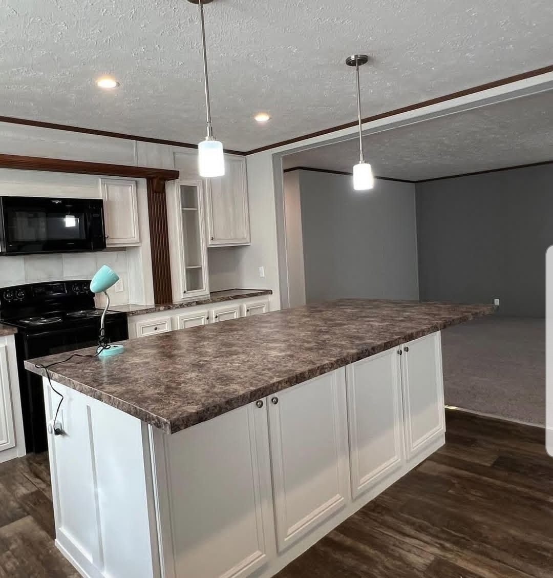 Modern kitchen with a large island featuring a marble countertop, white cabinets, and pendant lights. A black stove and a mint green lamp are visible, creating a sleek, inviting space.