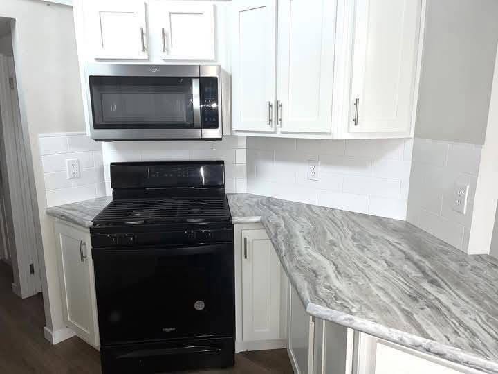 Modern kitchen with white cabinets, sleek silver microwave, black stove, and gray marble countertop. Bright, clean, and contemporary atmosphere.