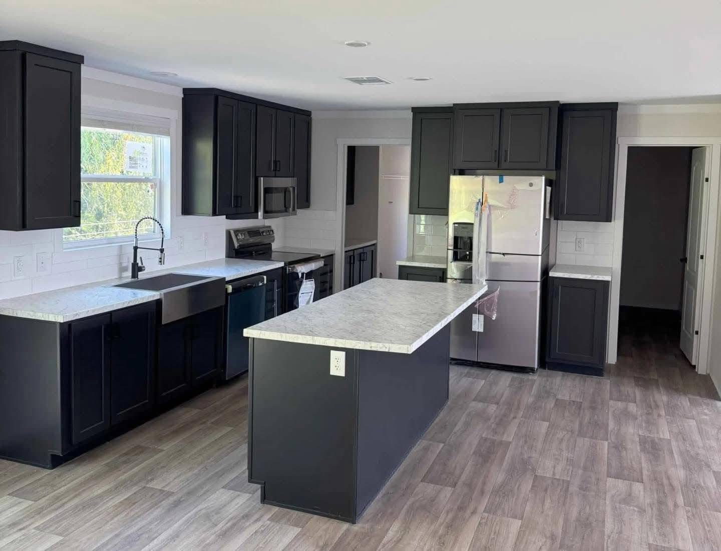 Modern kitchen with dark cabinets, stainless steel appliances, and a white countertop island. Light wood flooring creates a sleek, clean look.