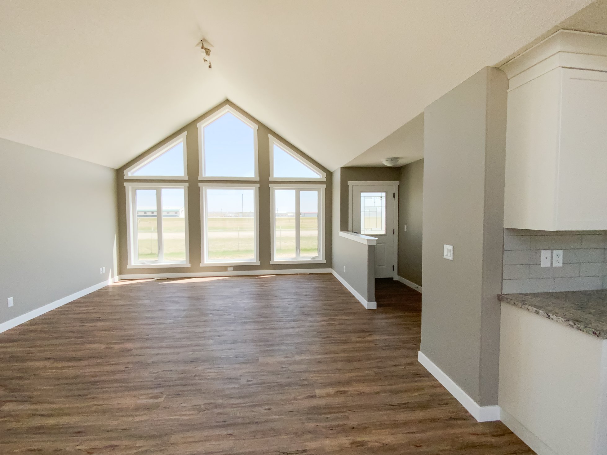 A spacious, empty room with a high, vaulted ceiling and large triangular windows that let in ample natural light, highlighting the wood flooring and neutral walls.