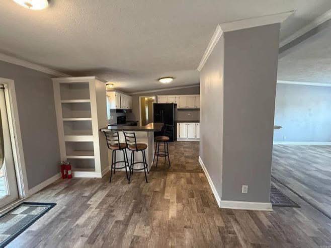 A modern kitchen with gray walls and wood floors features a breakfast bar with three stools, built-in shelves, white cabinets, and stainless steel appliances.