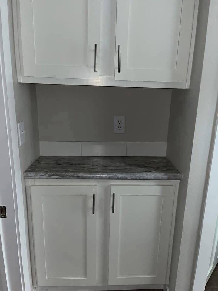 White kitchen cabinet with sleek silver handles, set against a gray wall. Marble countertop and an outlet, creating a modern, minimalist look.