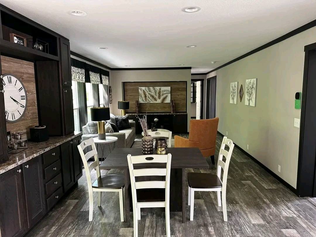 Modern living room with dark wood furniture, a wall clock, and a gray couch. An orange armchair and abstract art add color and style. Bright, cozy ambiance.