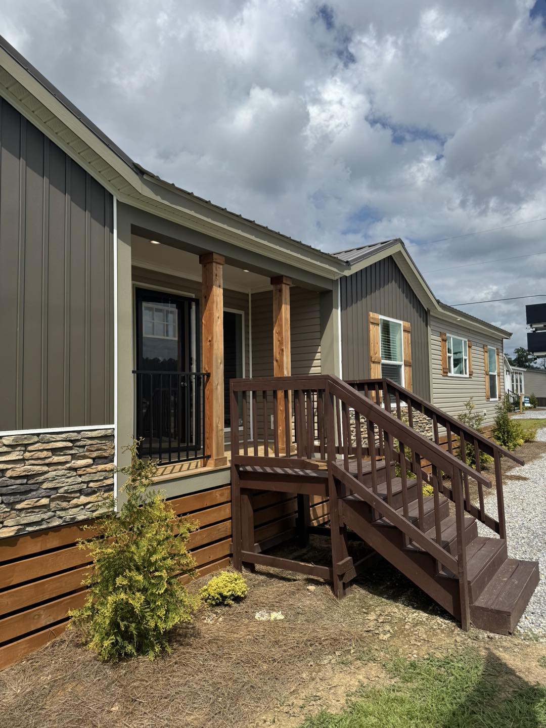 Single-story home with dark wood siding, stone accents, and a small porch with stairs. The sky is cloudy, creating a calm, overcast ambiance.